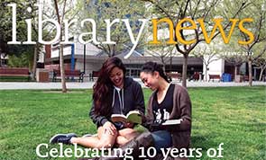 Photo of two students sitting on grass in front of the library building.